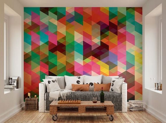 A colorful living room with geometric wall art. A couch with pillows and a wooden pallet coffee table.