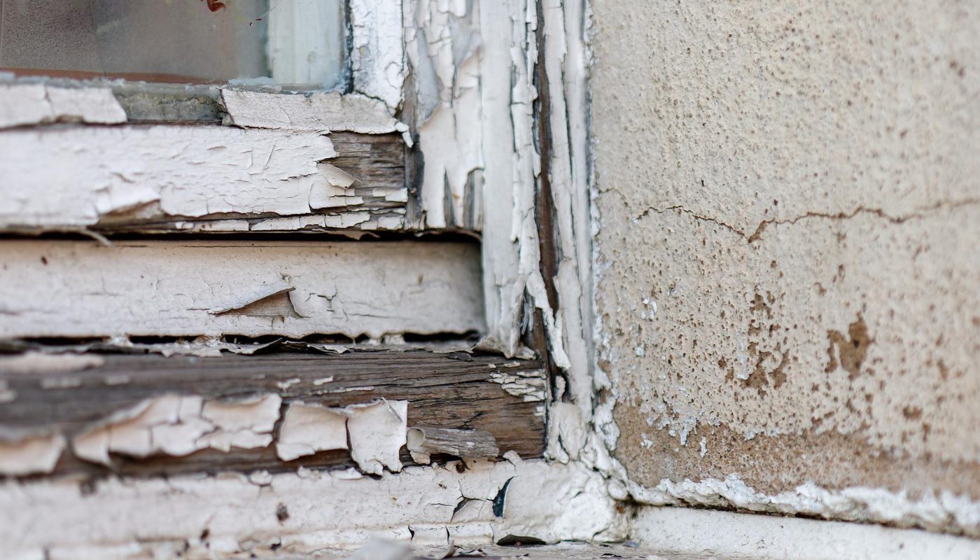 Peeling white paint on a weathered window frame and adjacent concrete wall.