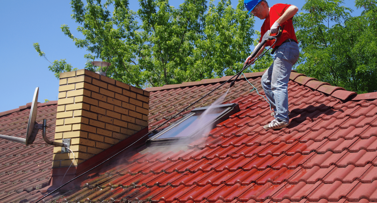 Man on a roof with a pressure washer hose