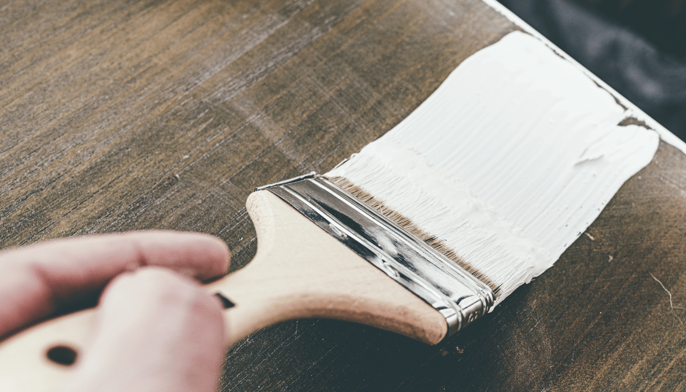 A person is holding a paint brush with white paint on it.