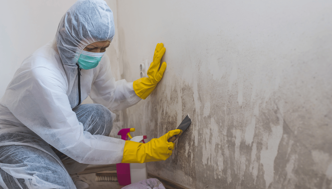 A person in a protective suit is cleaning a wall with a spatula.