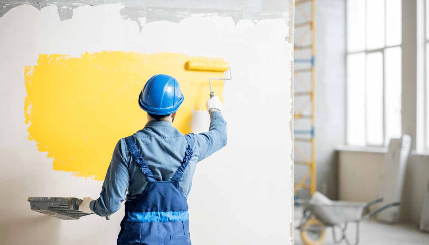 A man is painting a wall yellow with a roller.