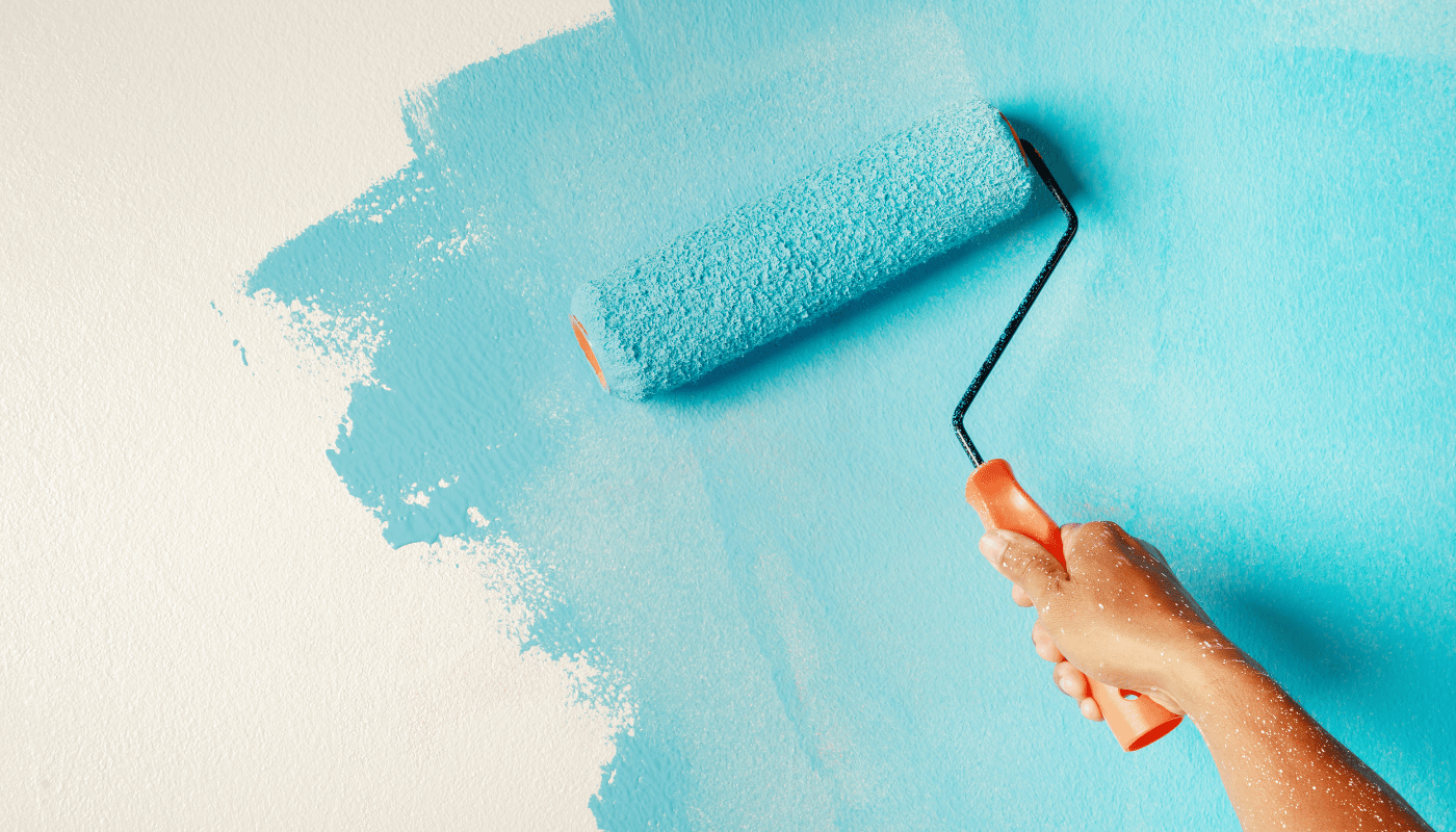 A person is painting a wall with a blue paint roller.