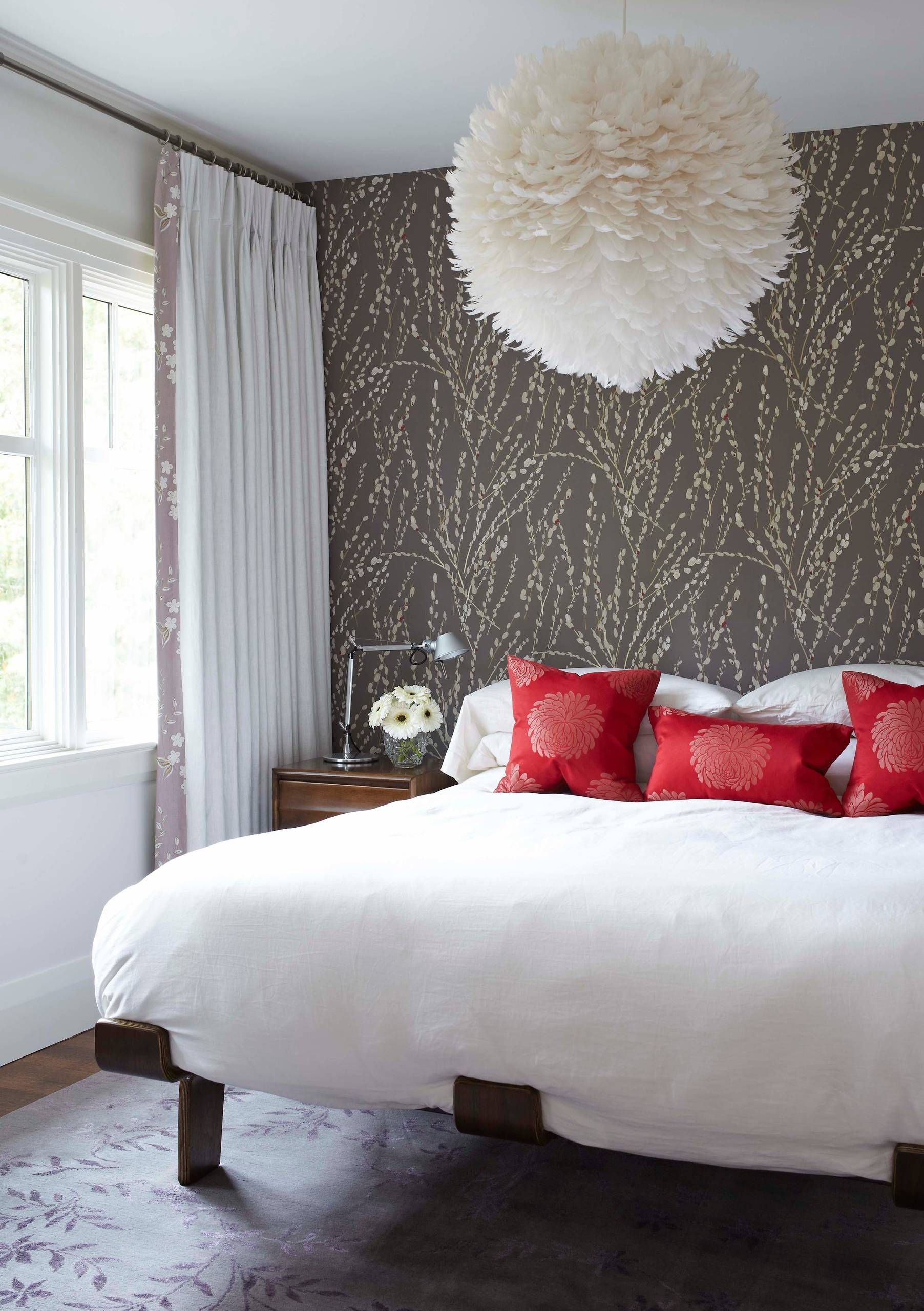 Bedroom with white bedding, red pillows, floral wallpaper, and large pendant light.