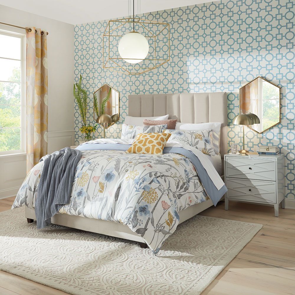 Bedroom with a floral comforter, geometric wallpaper, two mirrors, and a neutral-colored rug.