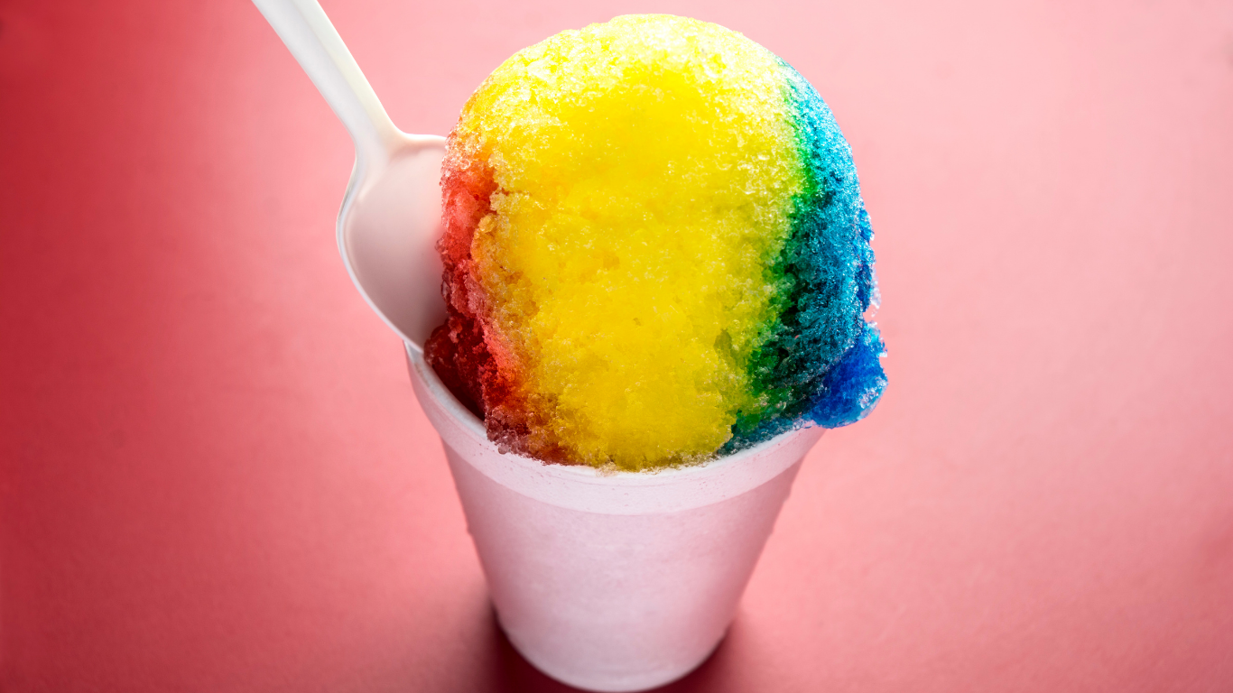 A rainbow colored shave ice in a styrofoam cup with a spoon.
