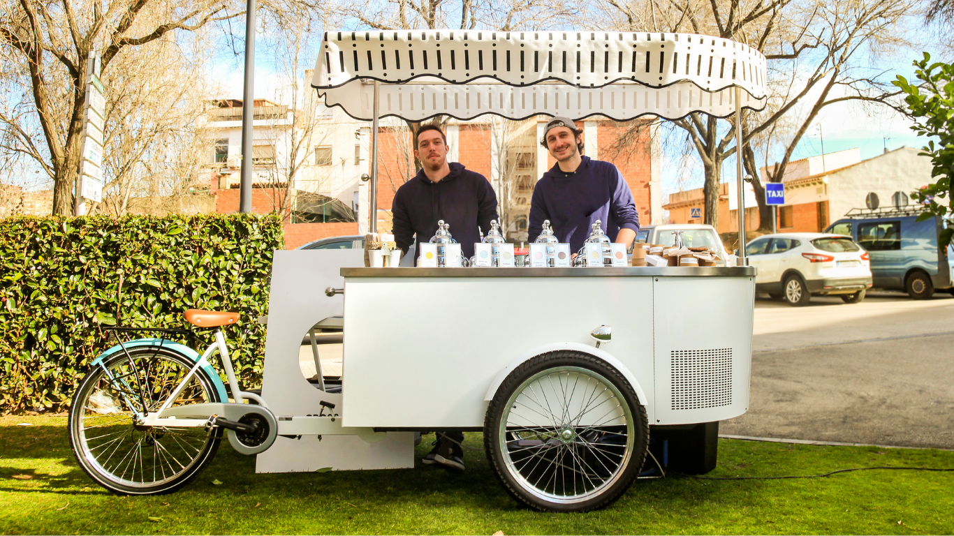 Two men are standing in front of a bicycle cart.
