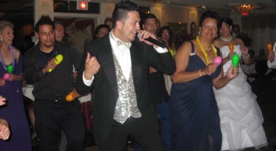 A man in a tuxedo is singing into a microphone at a party