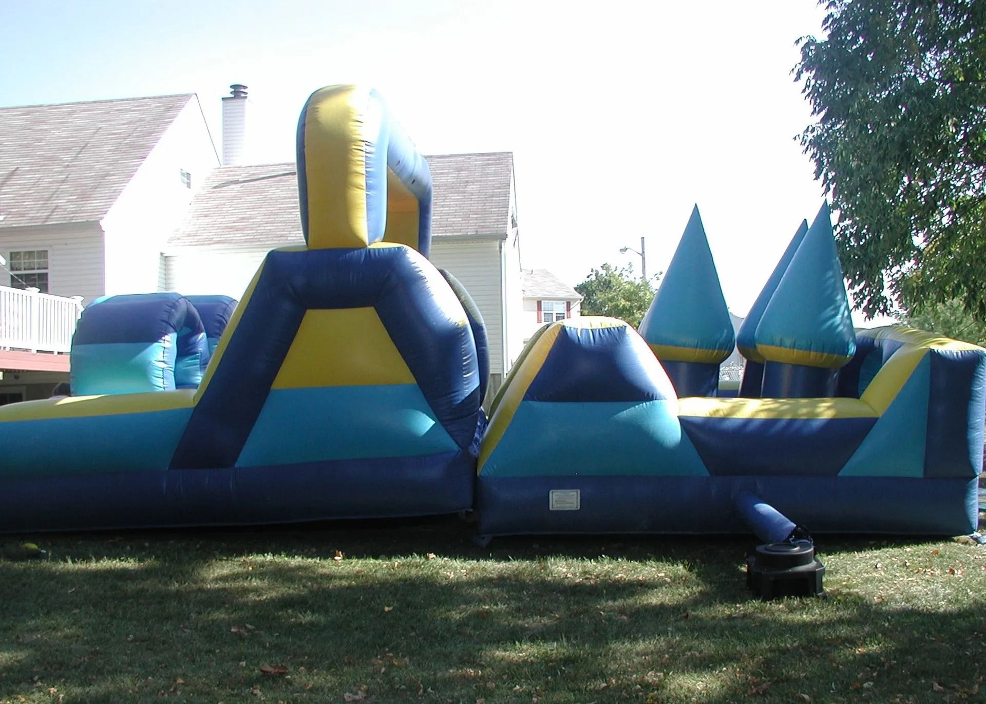 A blue and yellow bouncy house is sitting in the grass in front of a house