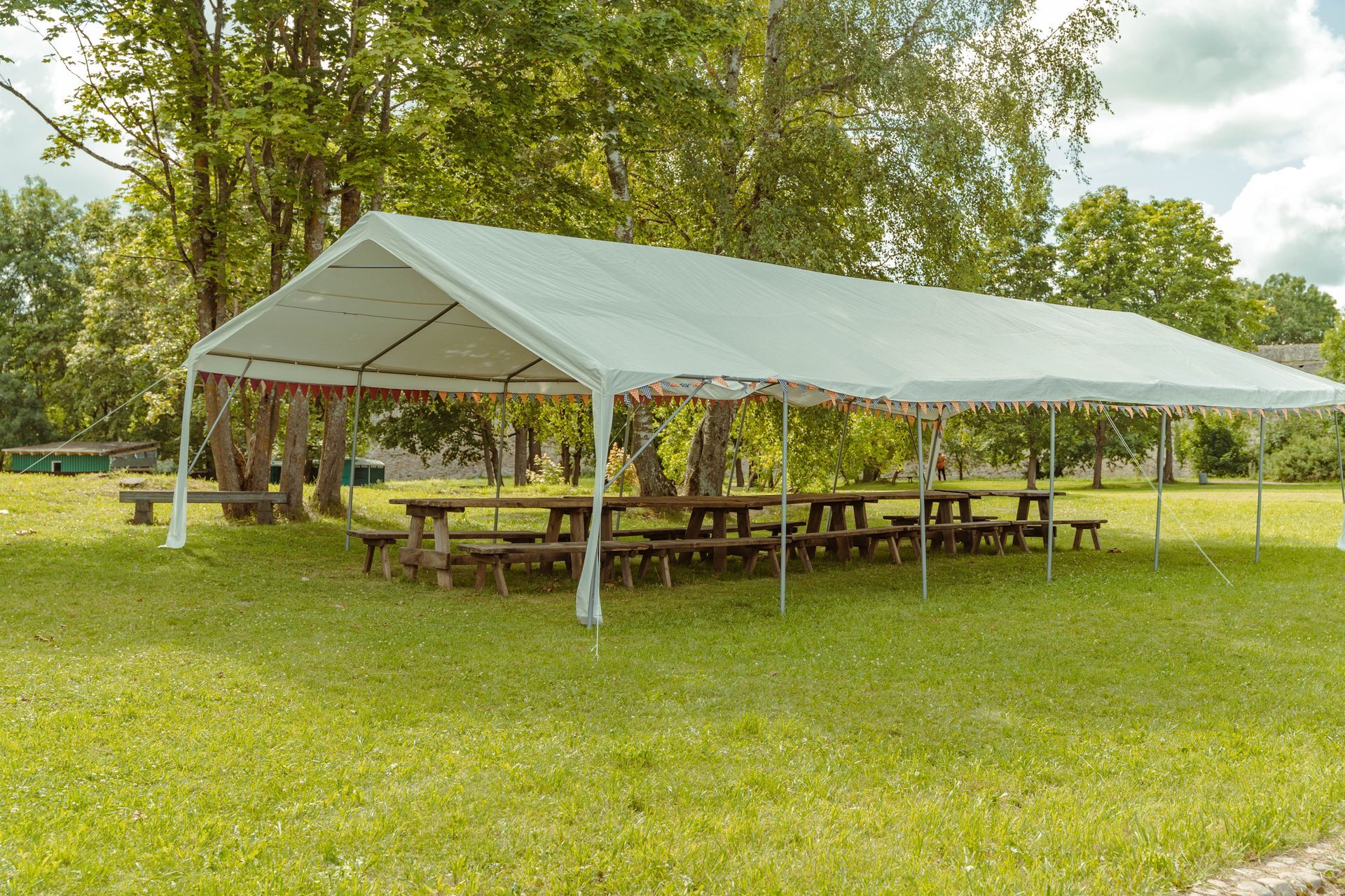 A large white tent with picnic tables underneath it in a grassy field.