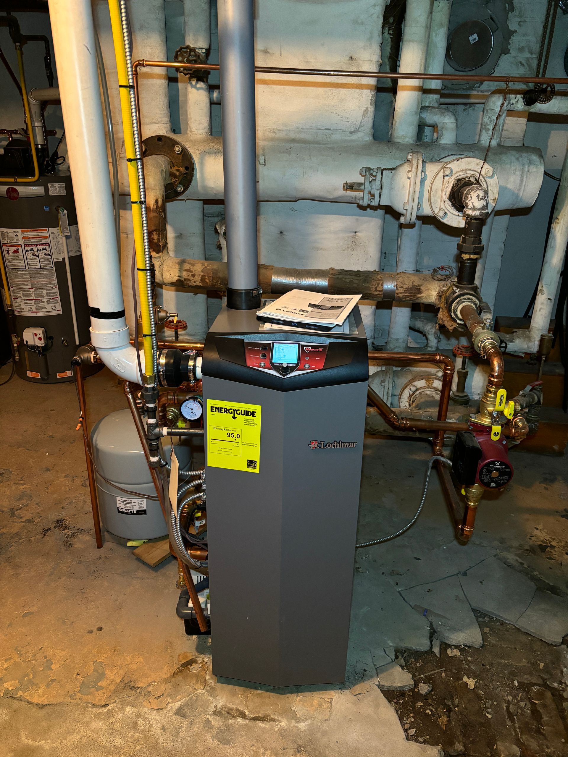 A gray furnace with copper pipes in a basement setting.