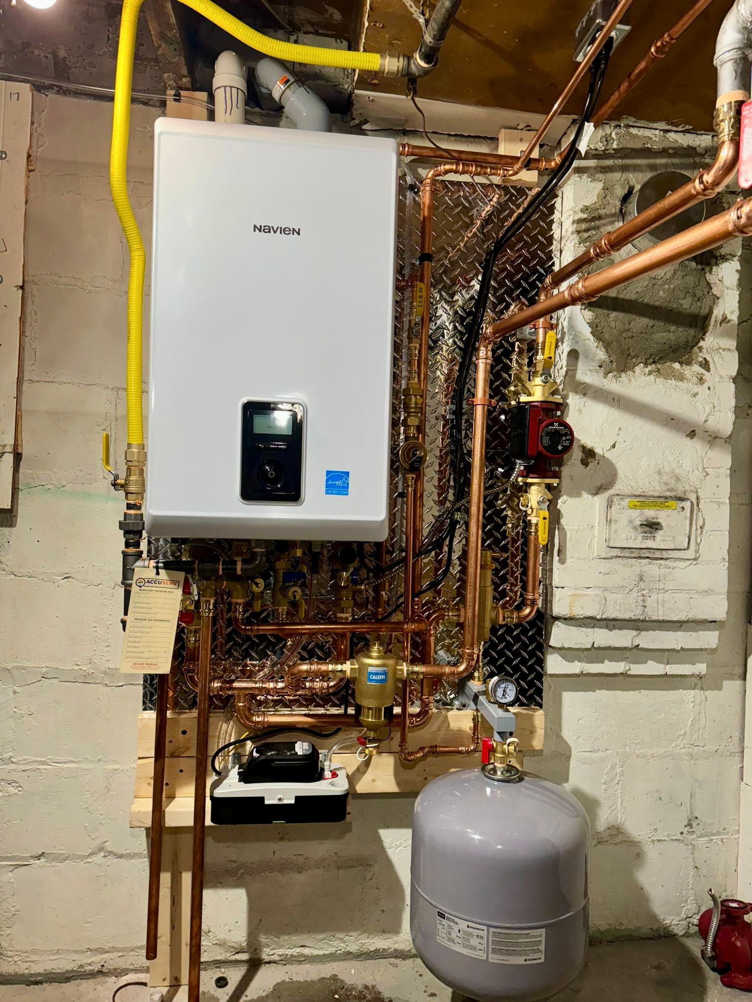 White wall-mounted boiler with copper pipes in a basement setting.