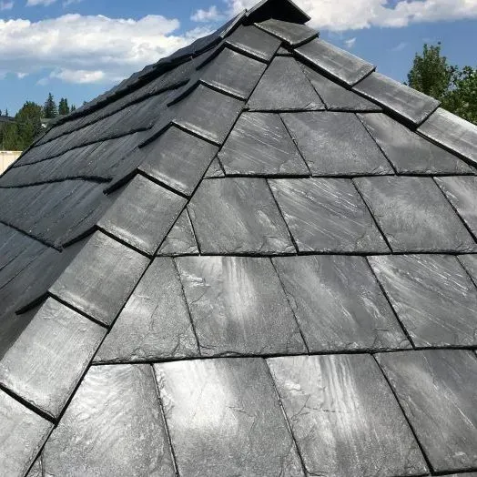 Worker spreading black roofing material on a flat roof with a yellow bucket nearby
