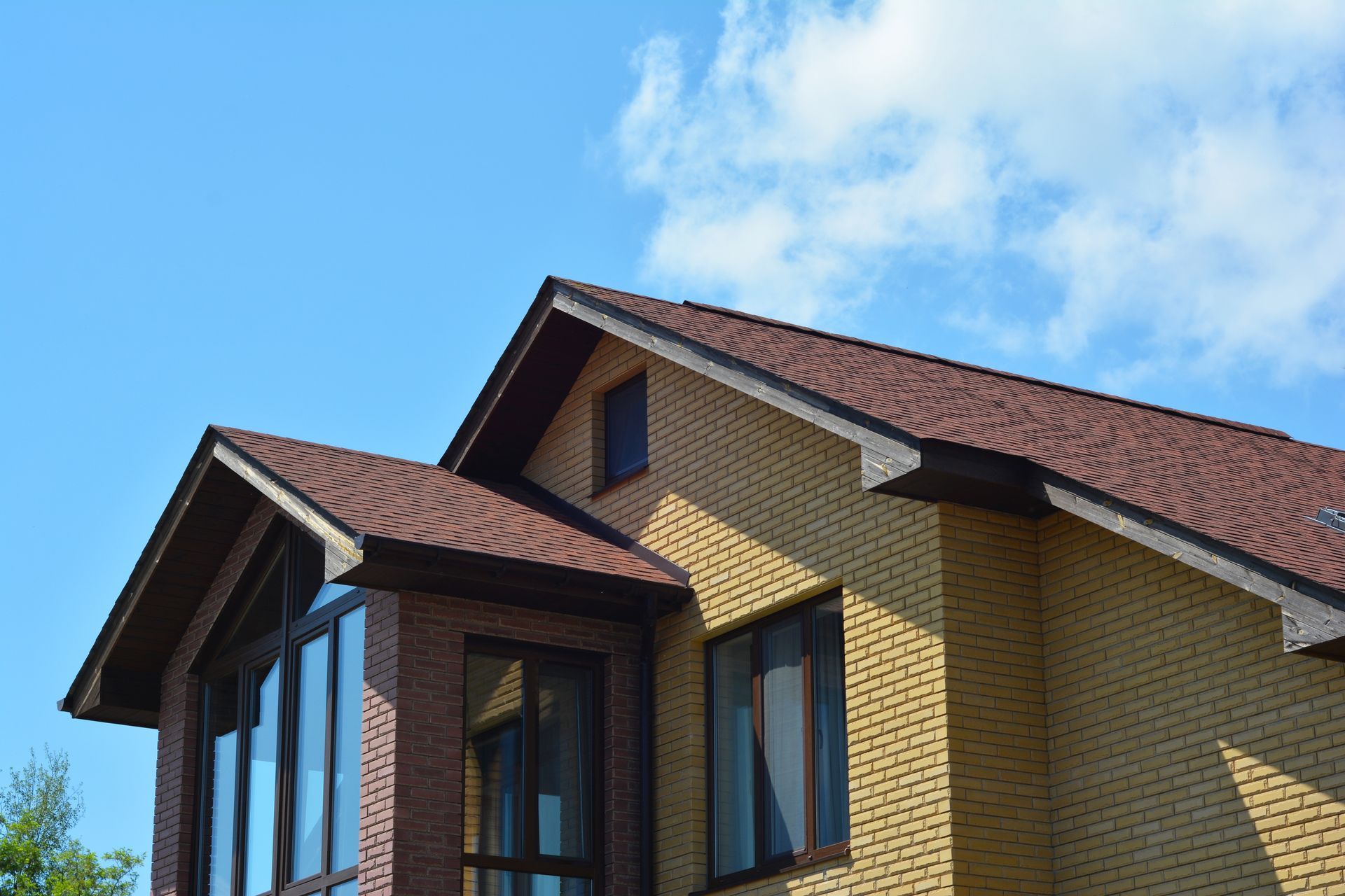 Yellow brick house with red roof and large windows under a bright blue sky