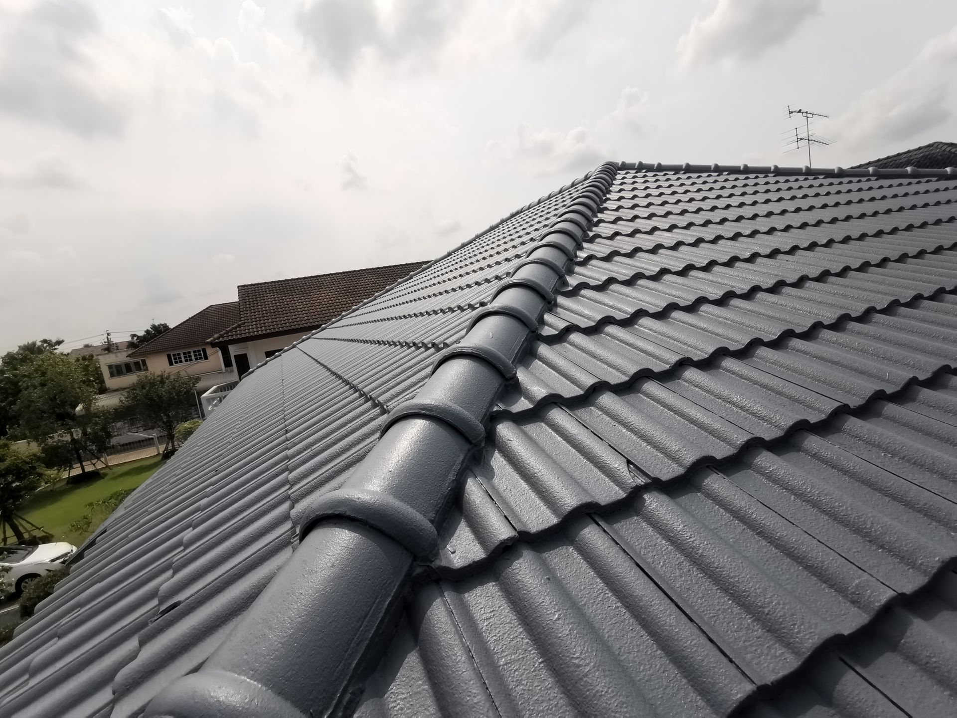Dark gray tiled roof with a ridge vent under a cloudy sky, viewed from above.
