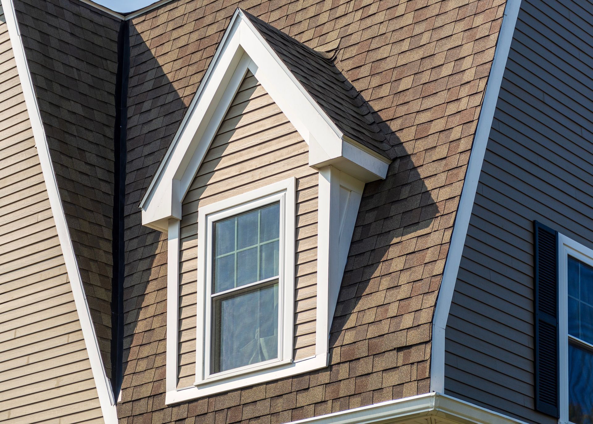 Dormer window with white trim on a brown shingled house roof