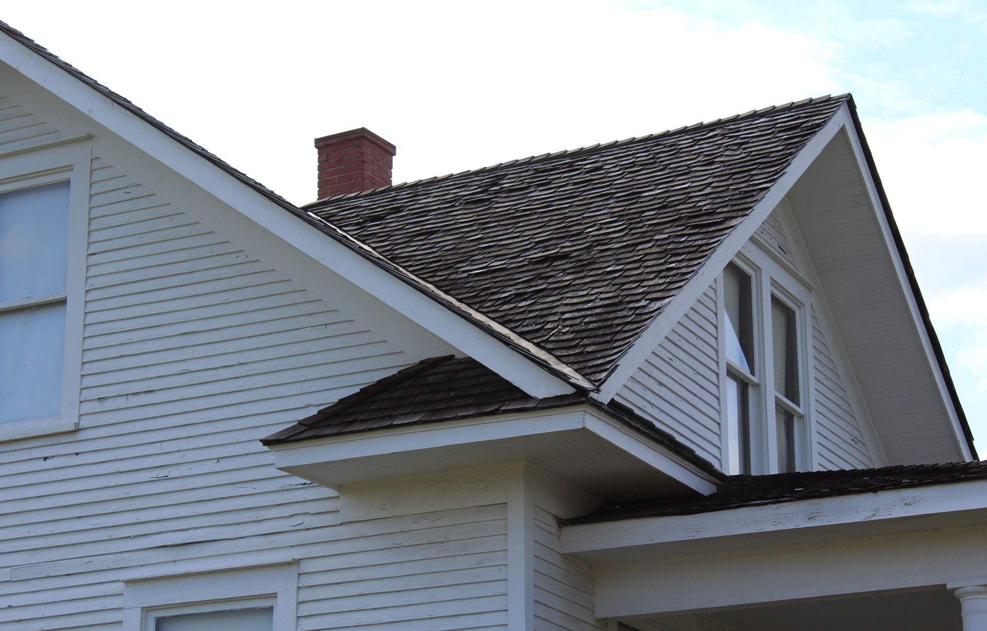 White house exterior with a steep gabled roof and chimney under a cloudy sky