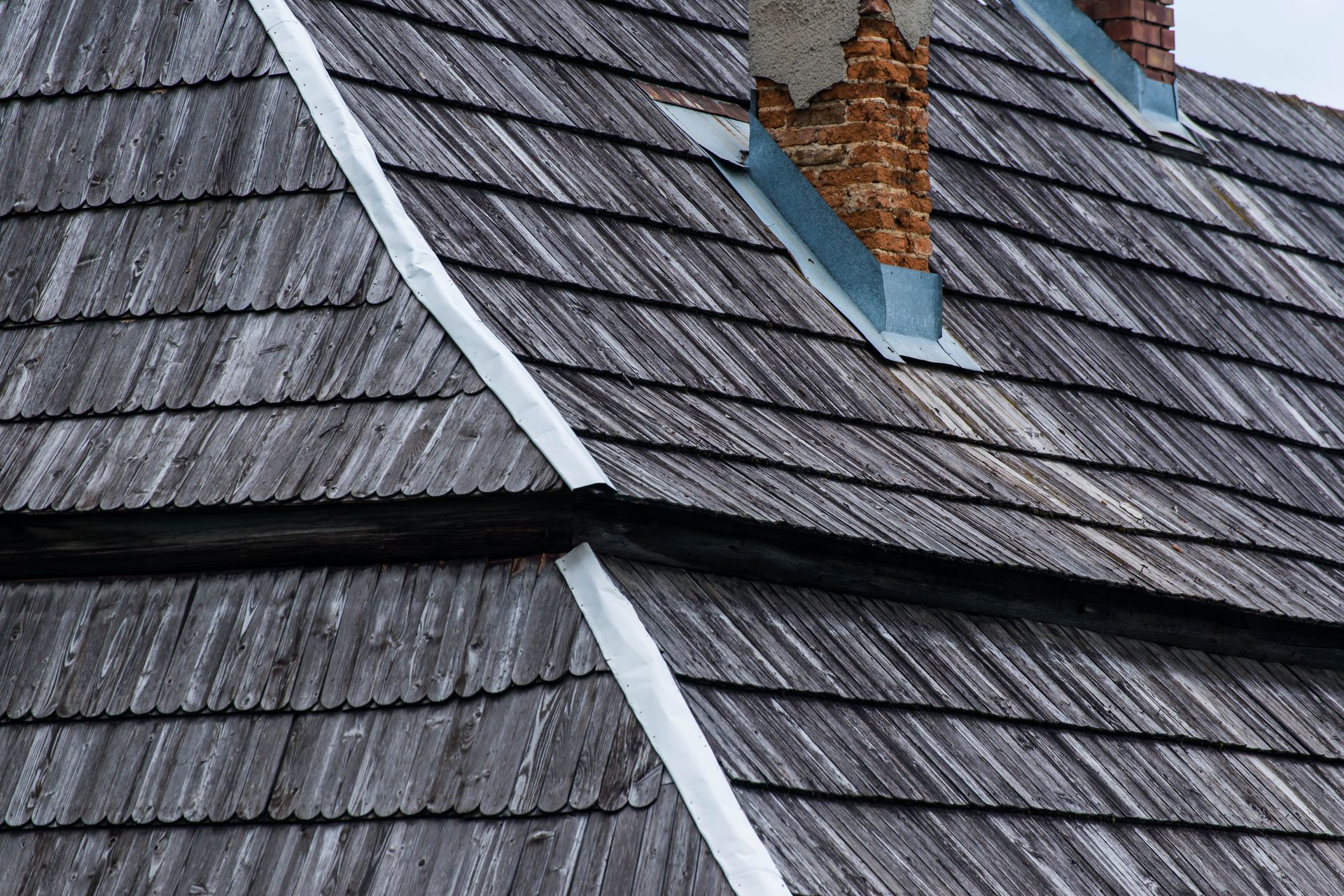 Gray shingle roof with a chimney and white flashing, showing a wet or weathered surface