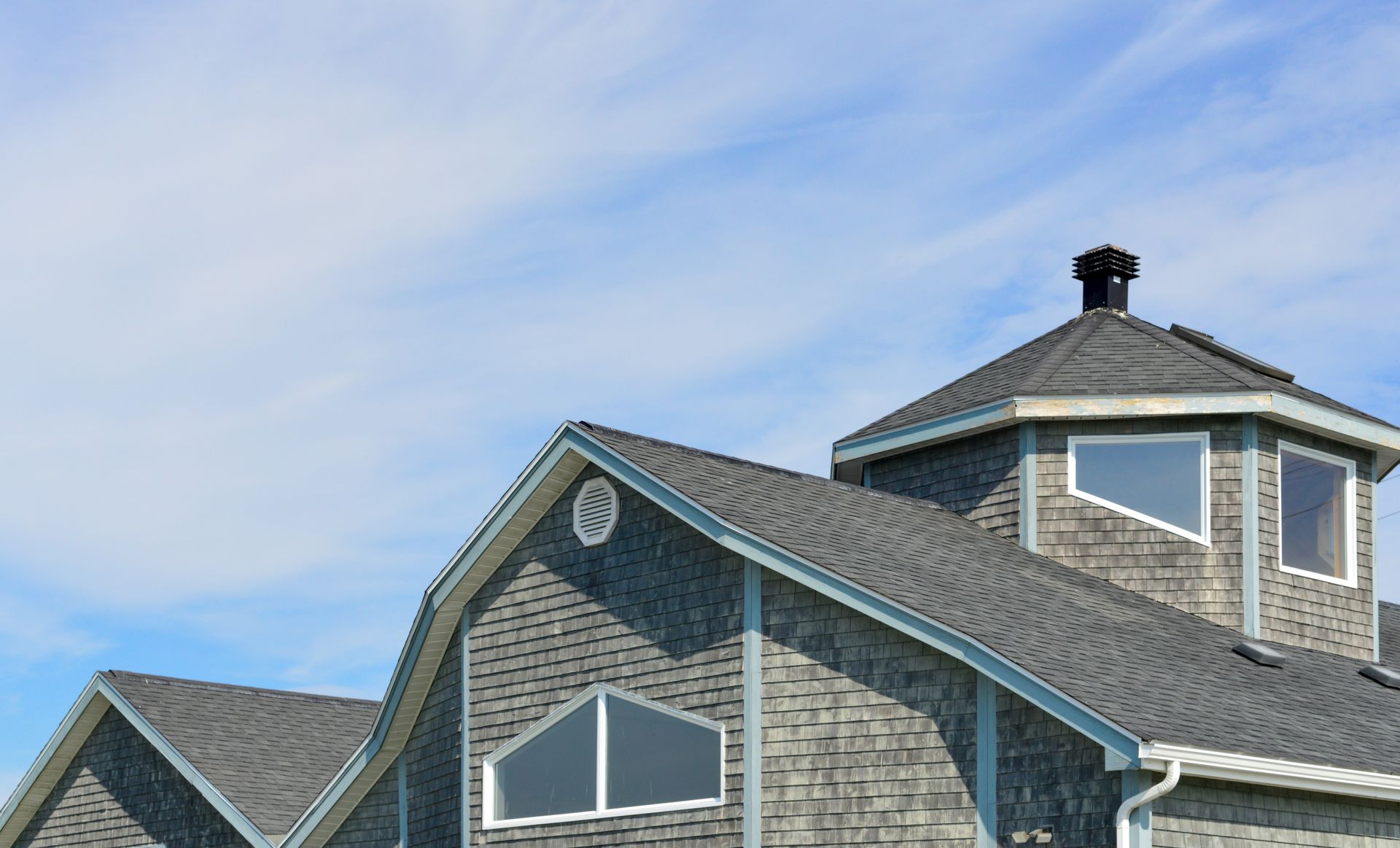 Blue-gray shingled house roof with dormer windows under a cloudy sky