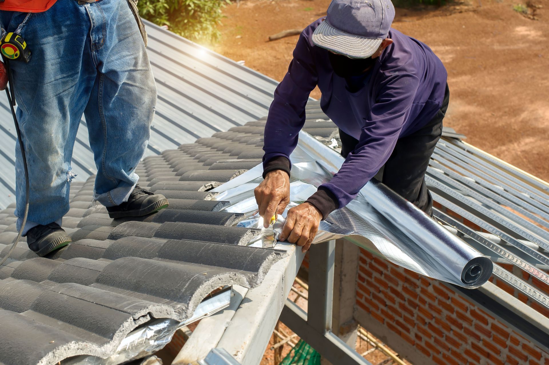 Two workers installing metal roofing on a house, bending and securing a silver panel.