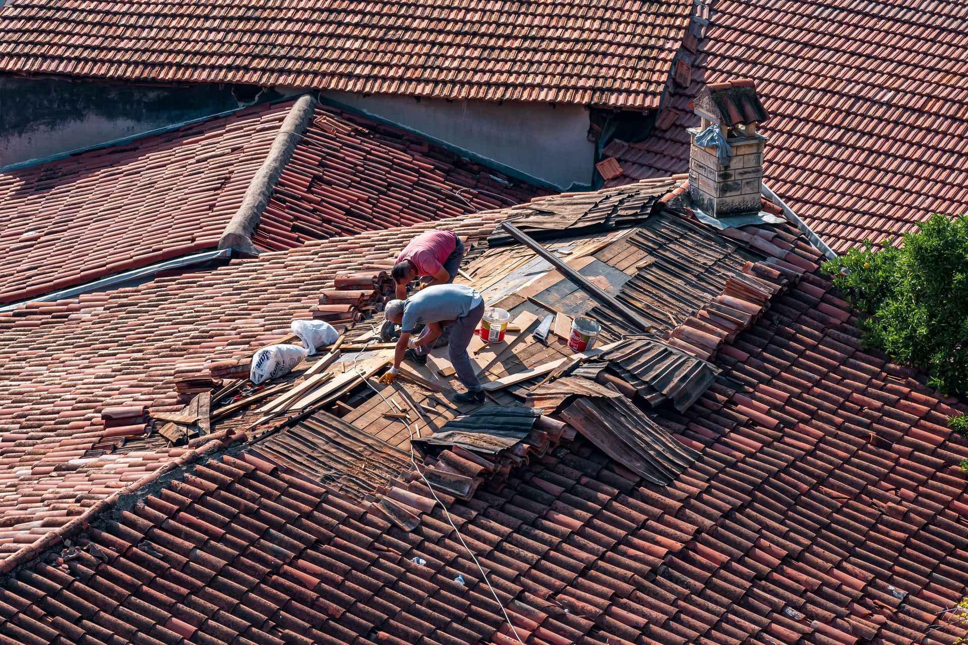 Workers repairing damaged roof tiles on a red-tiled house roof