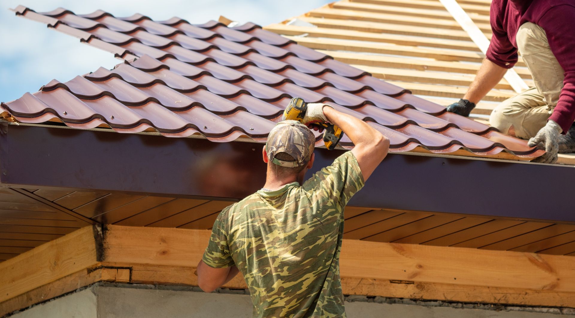 Two roofers working on a tiled roof, one standing on the roof and one below passing materials.