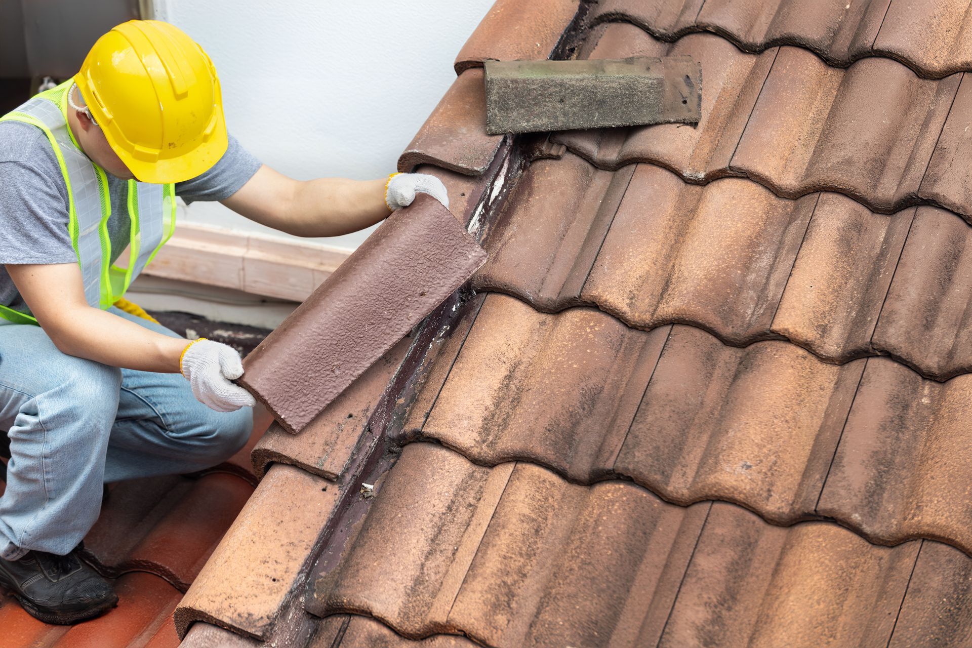 Worker in a yellow hard hat applying sealant to a tiled roof