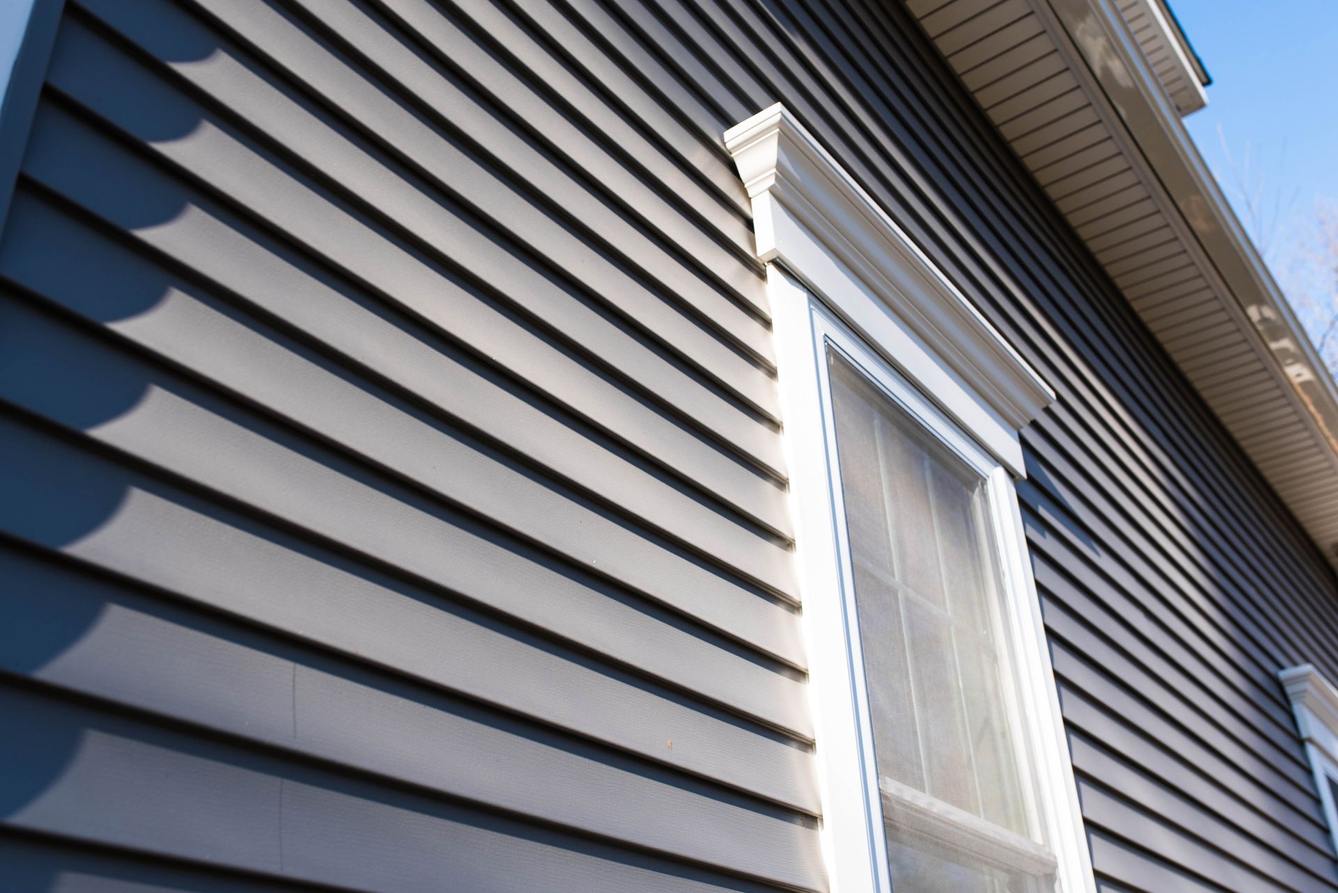 Gray vinyl house siding with a white-trimmed window under the roof eaves