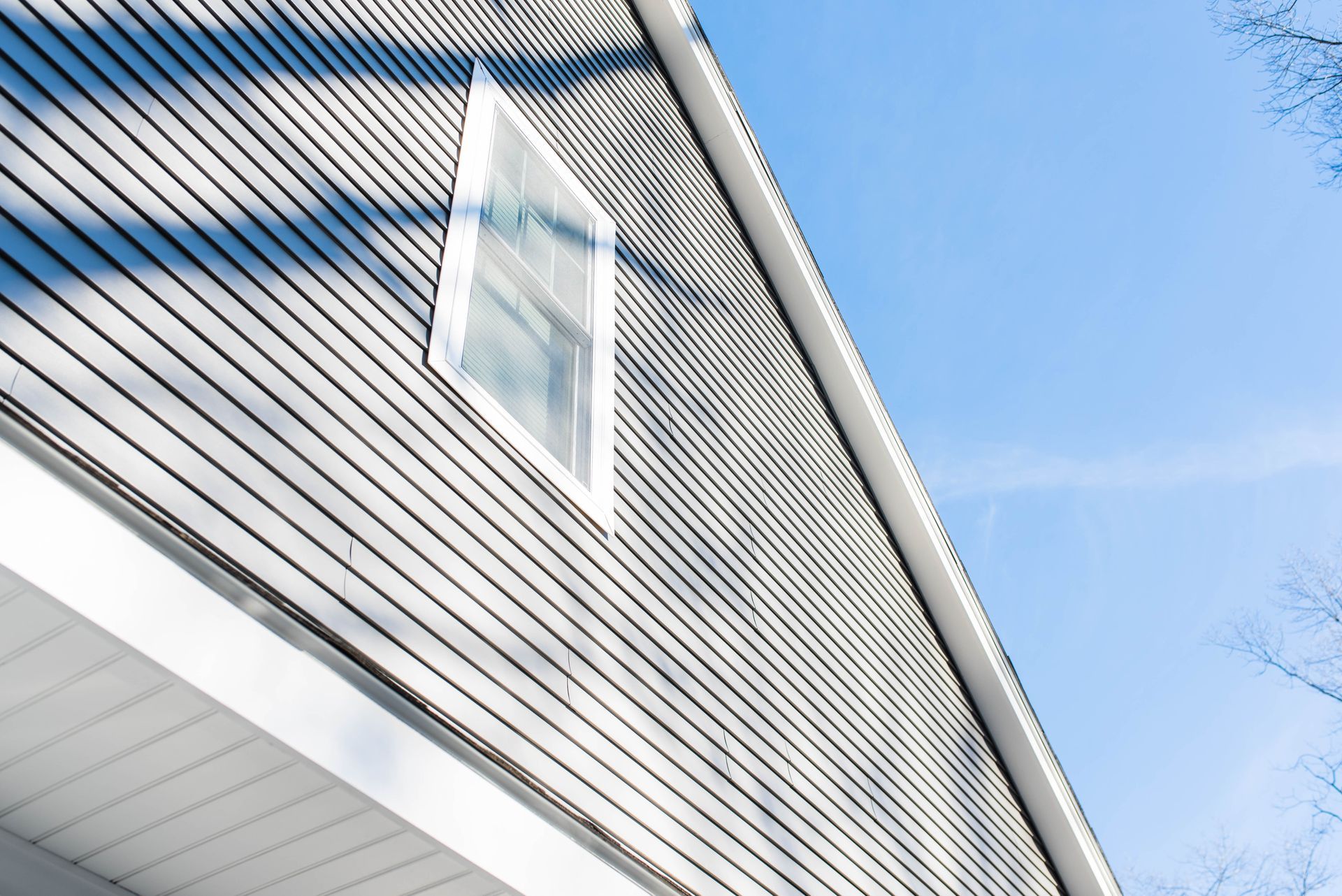 Close-up of a gray house exterior with a white-trimmed window against a blue sky
