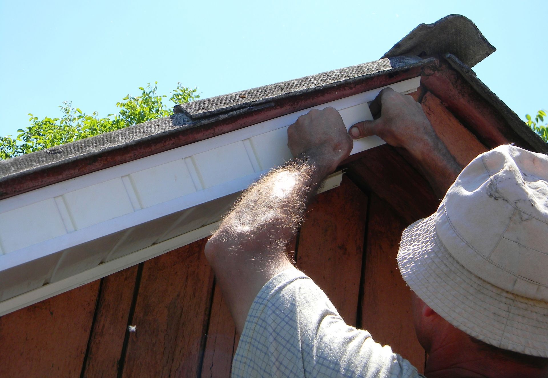 Person installing roofing under a red roof eave on a sunny day