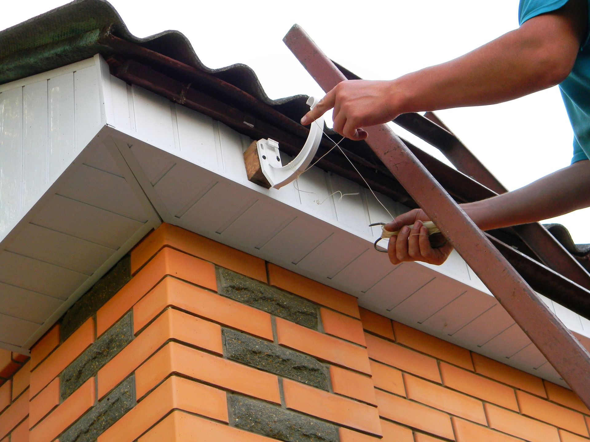 Worker installing rain gutter on a house roof corner