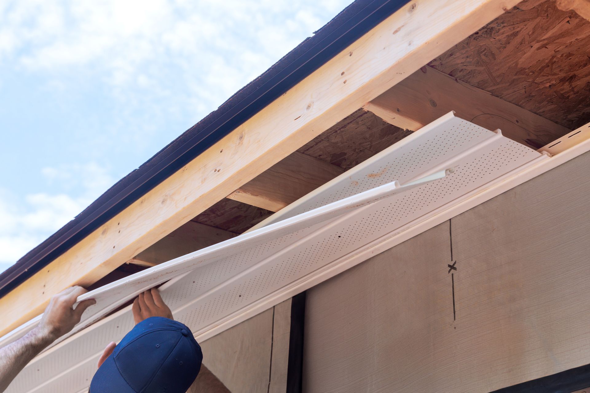 Person installing white soffit panels under a roof eave outdoors