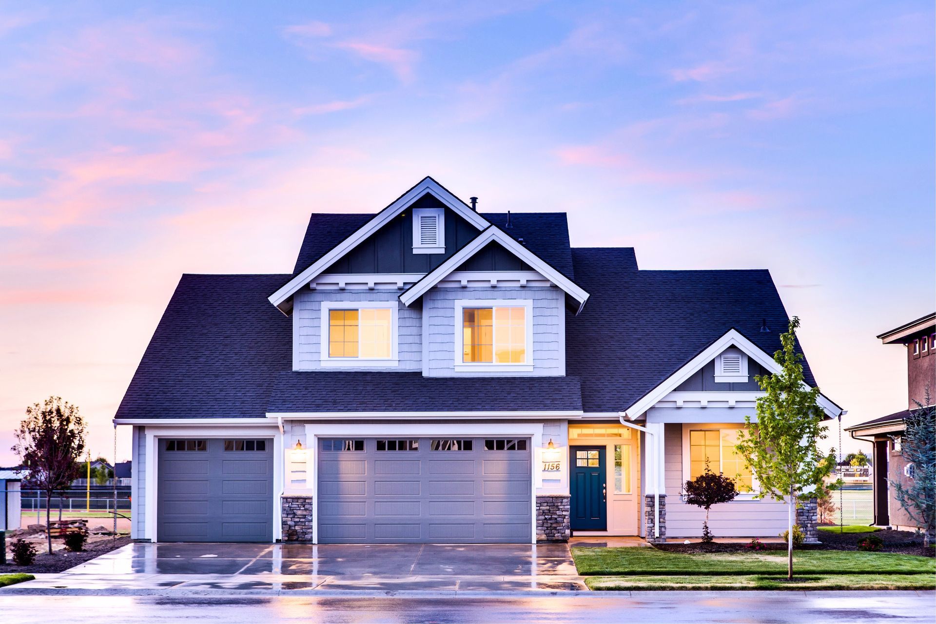 Two-story gray house with lit windows and garage at dusk under a pink sky