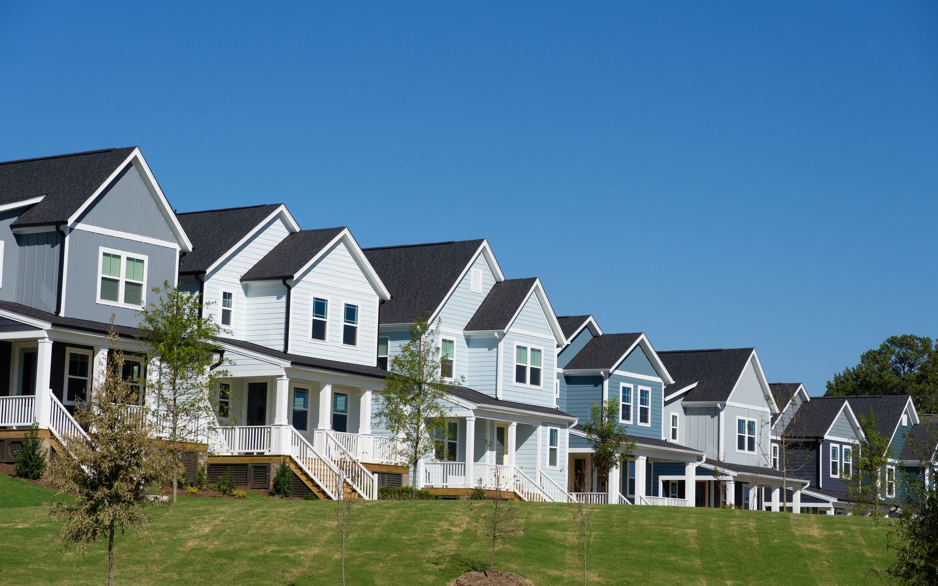 Row of modern white and gray suburban houses with porches under a clear blue sky.