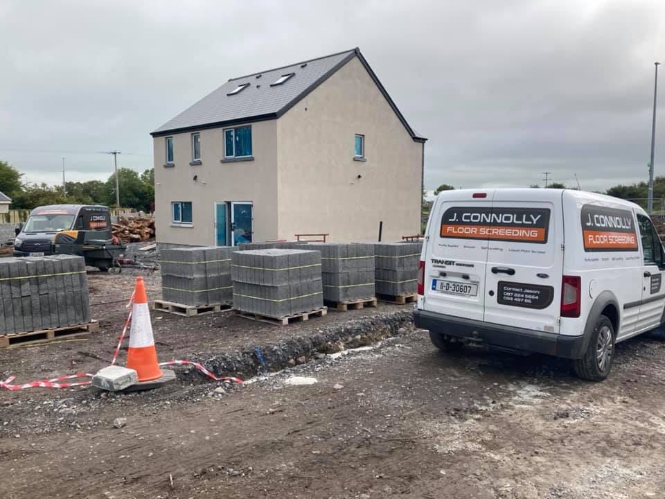 A white van is parked in front of a house under construction.