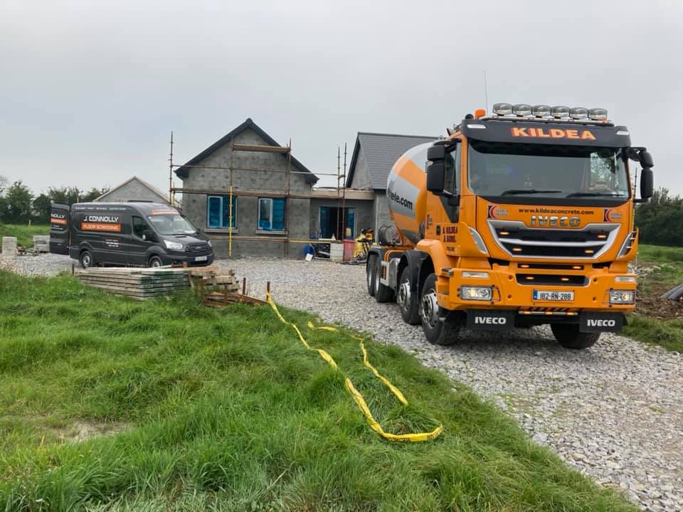 A concrete mixer truck is parked in front of a house under construction.