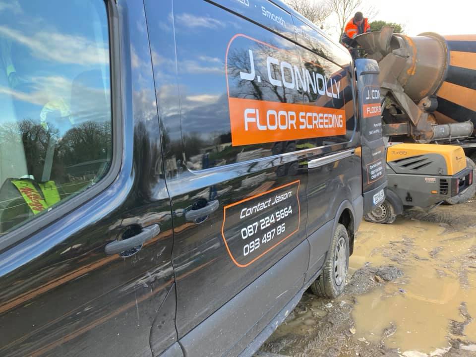 A black van is parked next to a concrete mixer on a muddy road.