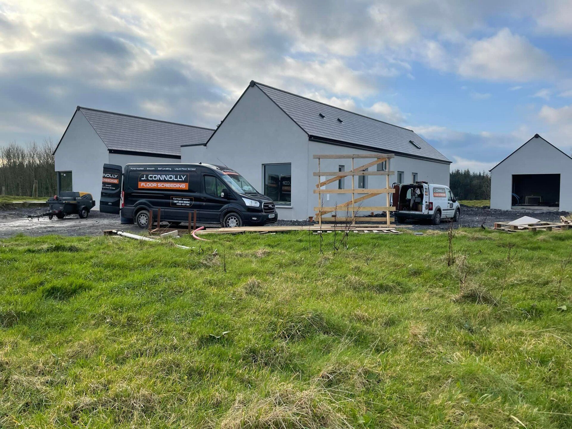 Two vans are parked in front of a house under construction.
