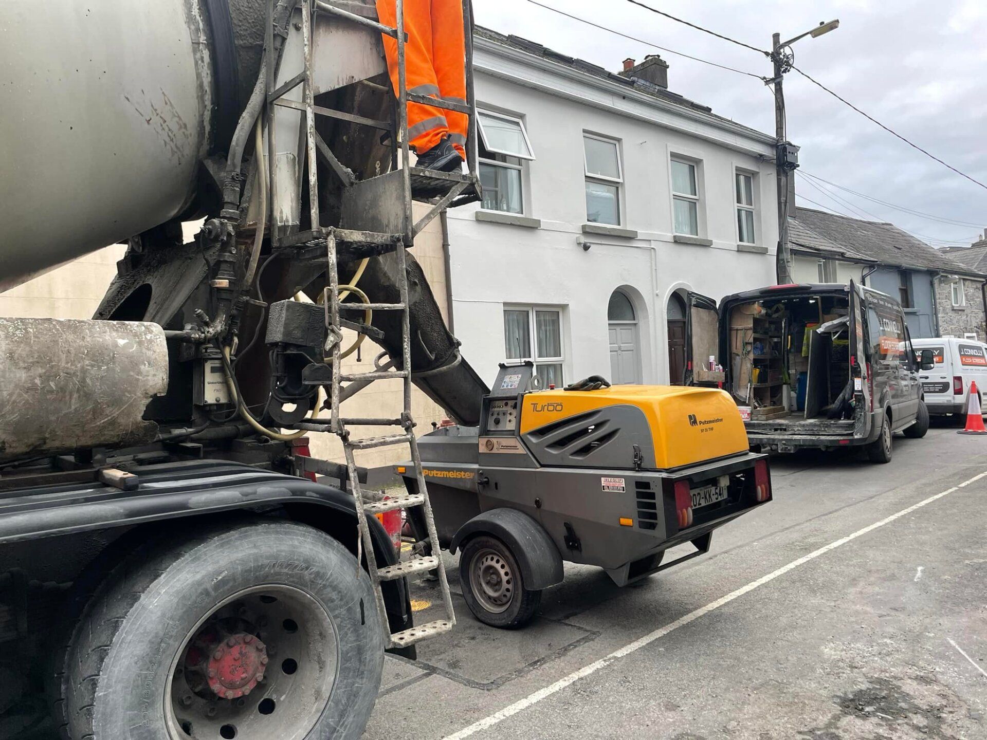 A concrete mixer truck is parked on the side of the road in front of a building.