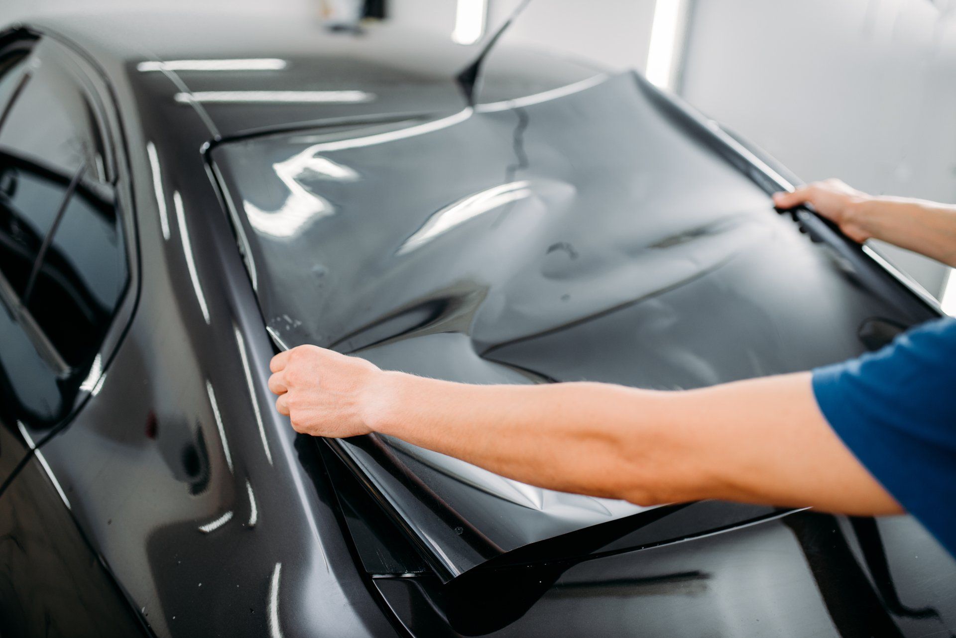 A man is applying tinted window film to a black car.