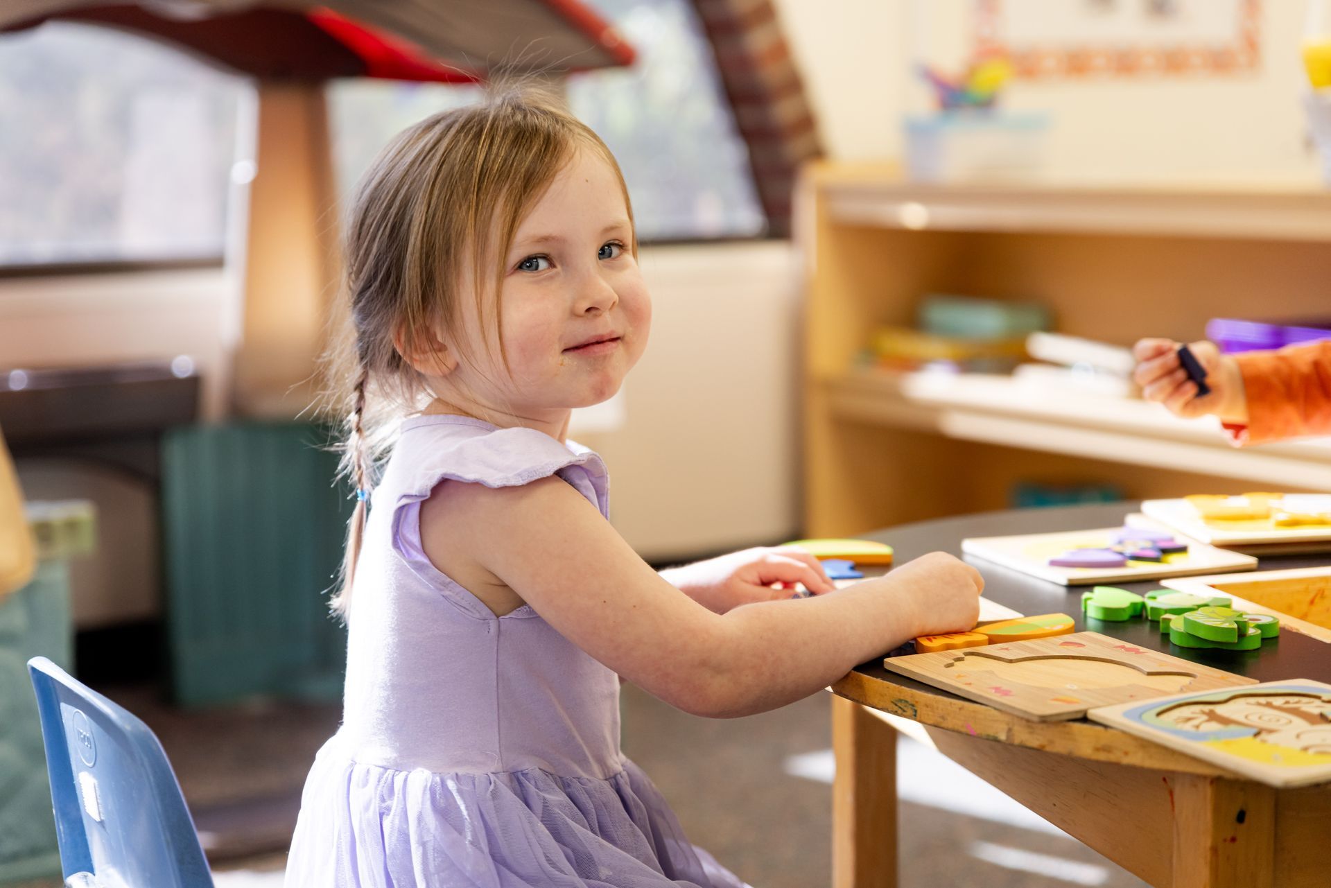 A little girl in a purple dress is sitting at a table in a classroom.