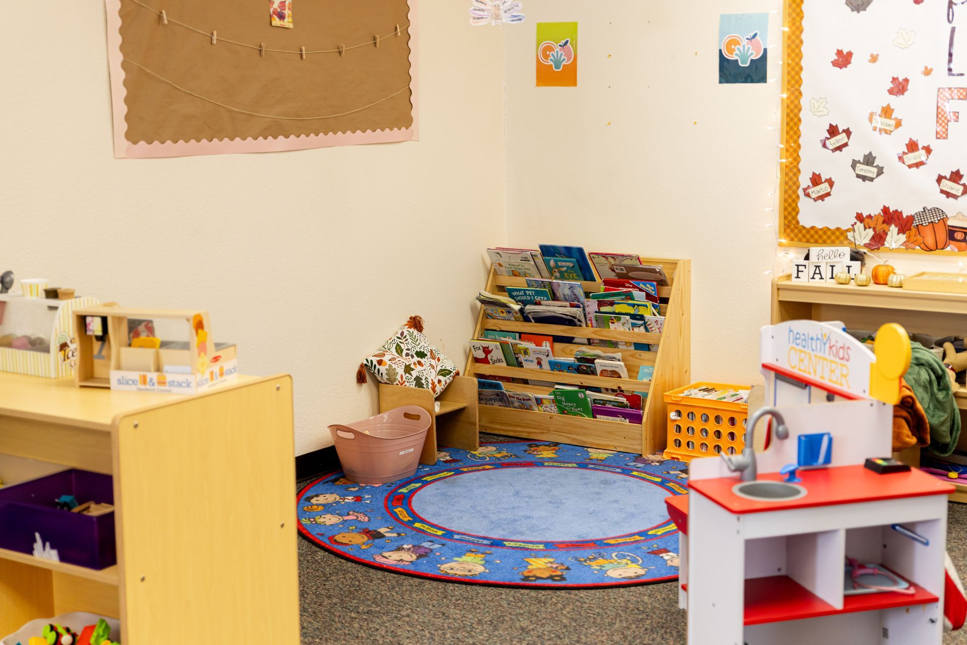 A room with a rug , bookshelves , and a toy kitchen.
