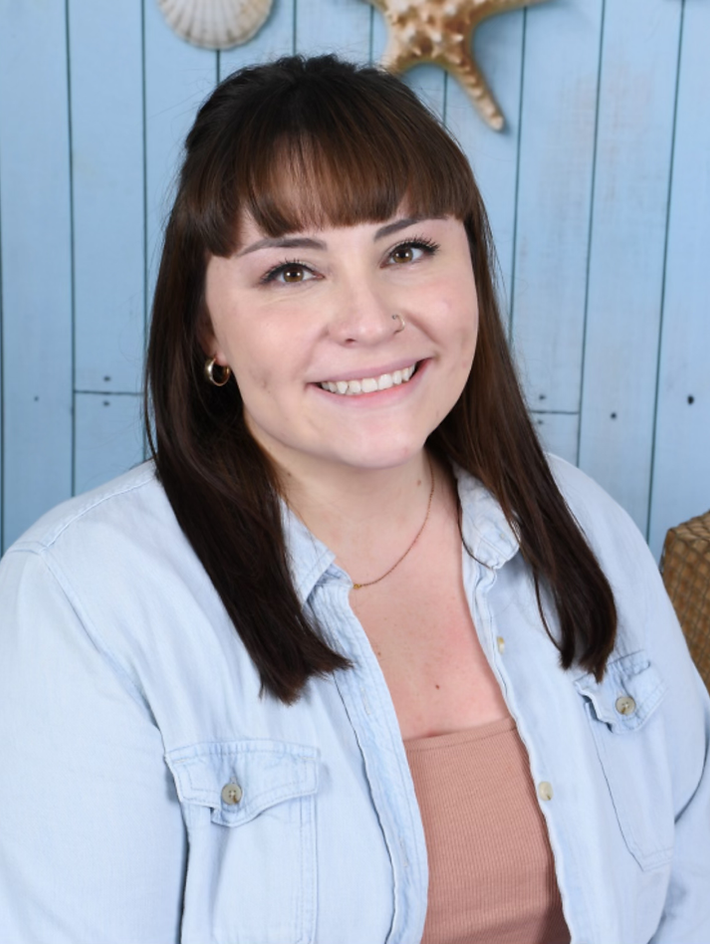 A woman is smiling in front of a blue wall with seashells on it.