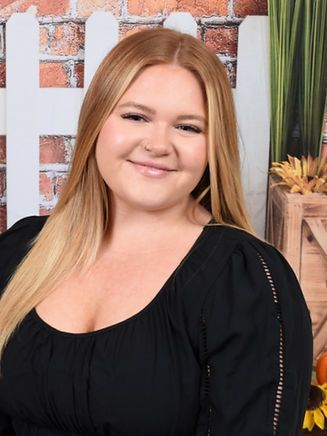 A woman in a black top is smiling in front of a white picket fence.