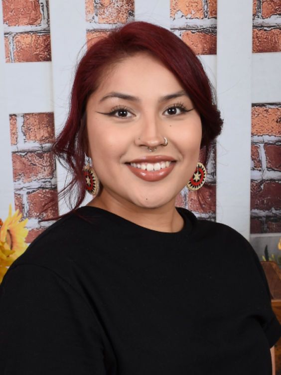 A woman with red hair and earrings is smiling in front of a brick wall.