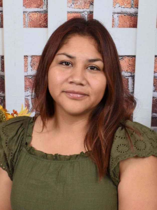 A woman in a green shirt is standing in front of a white fence.
