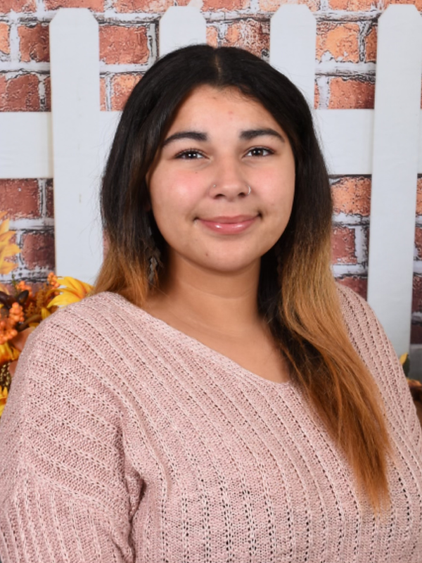 A woman in a pink sweater is standing in front of a white picket fence.