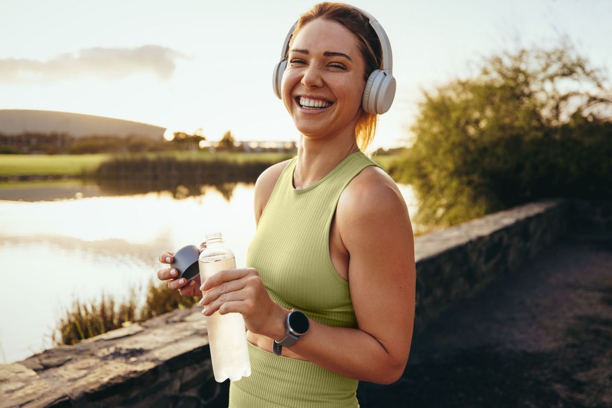 photo of a woman wearing a green tank top and headphones having a water break during her run
