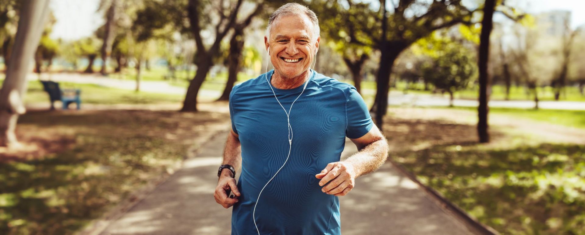 senior white man in blue shirt running in park