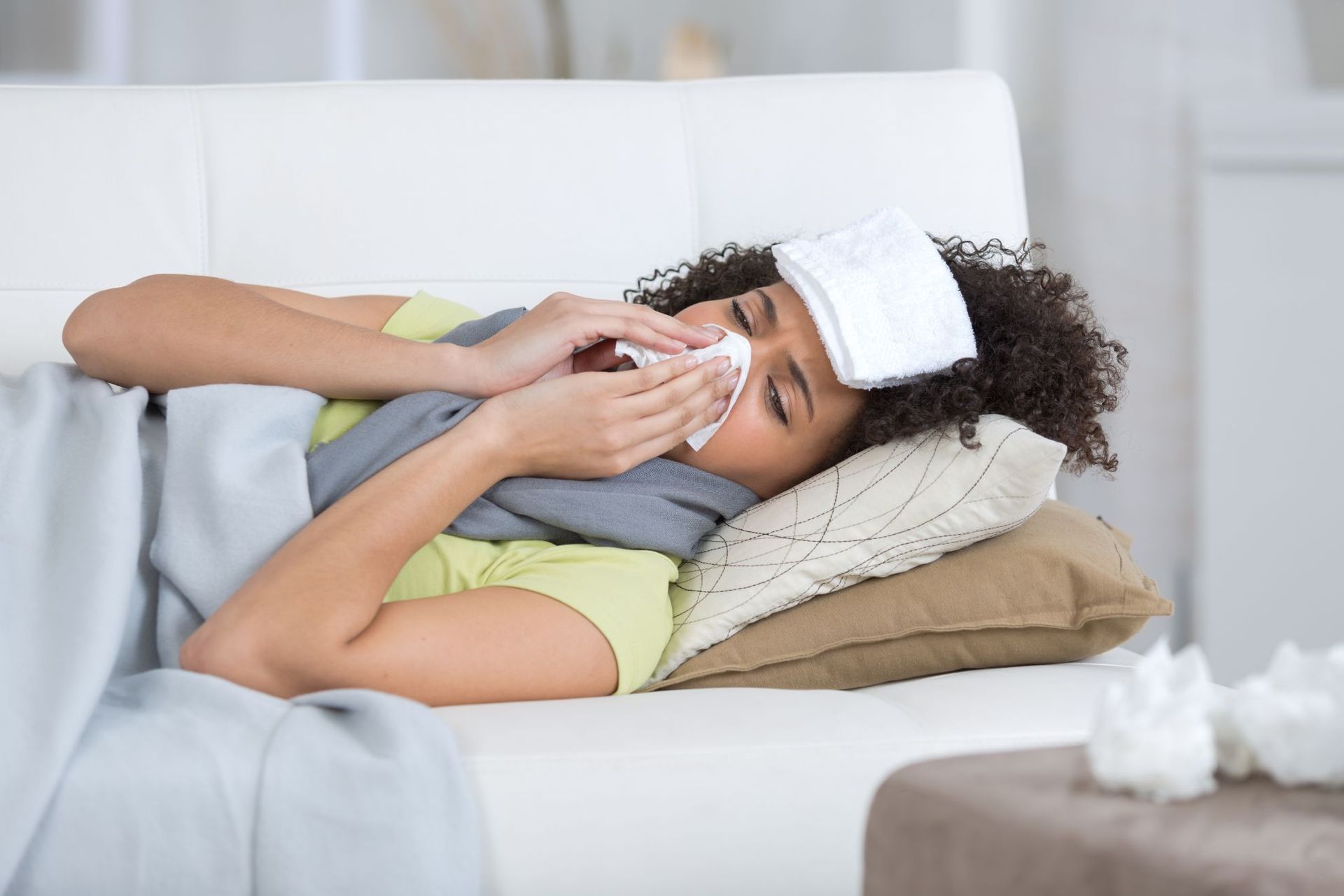 sick young woman laying on sofa blowing nose
